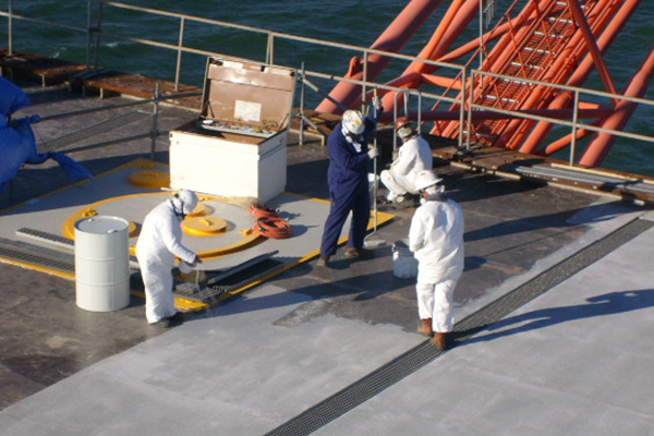 Four workers wearing safety gear applying deck coating on an offshore platform field installation